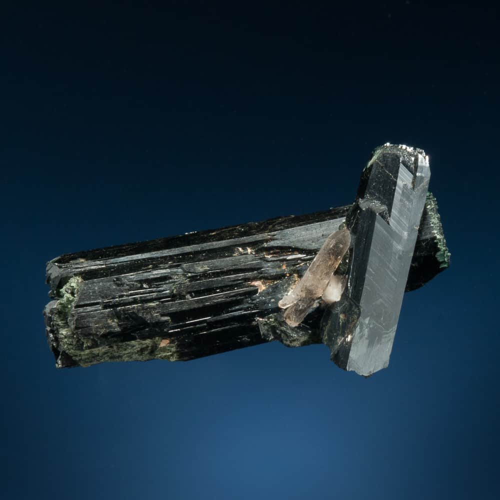 Dos cristales de aegirina afilados, lustrosos e intercalados con un cristal de cuarzo